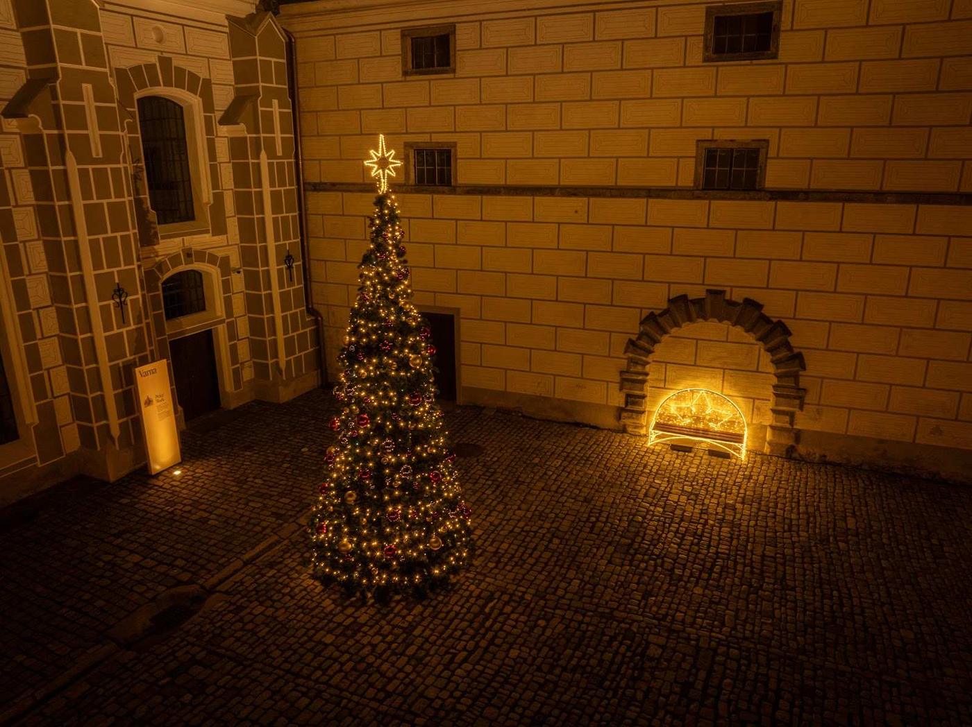 Osvětlený vánoční strom se špičkou ve tvaru hvězdy a světelná lavička na dlážděném nádvoří.